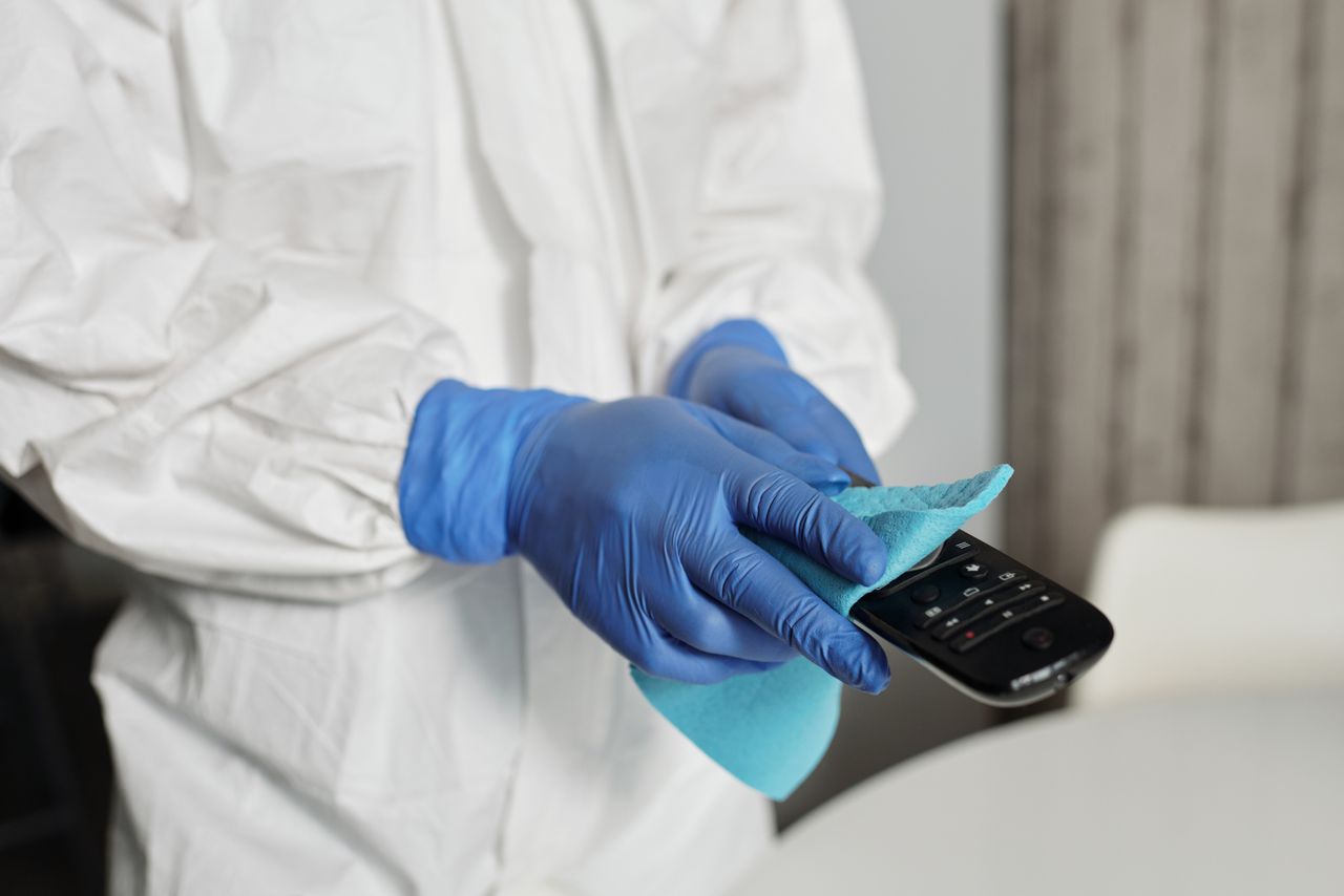 Gros plan d’une personne désinfectant une télécommande avec des gants de protection, afin de garantir la propreté.